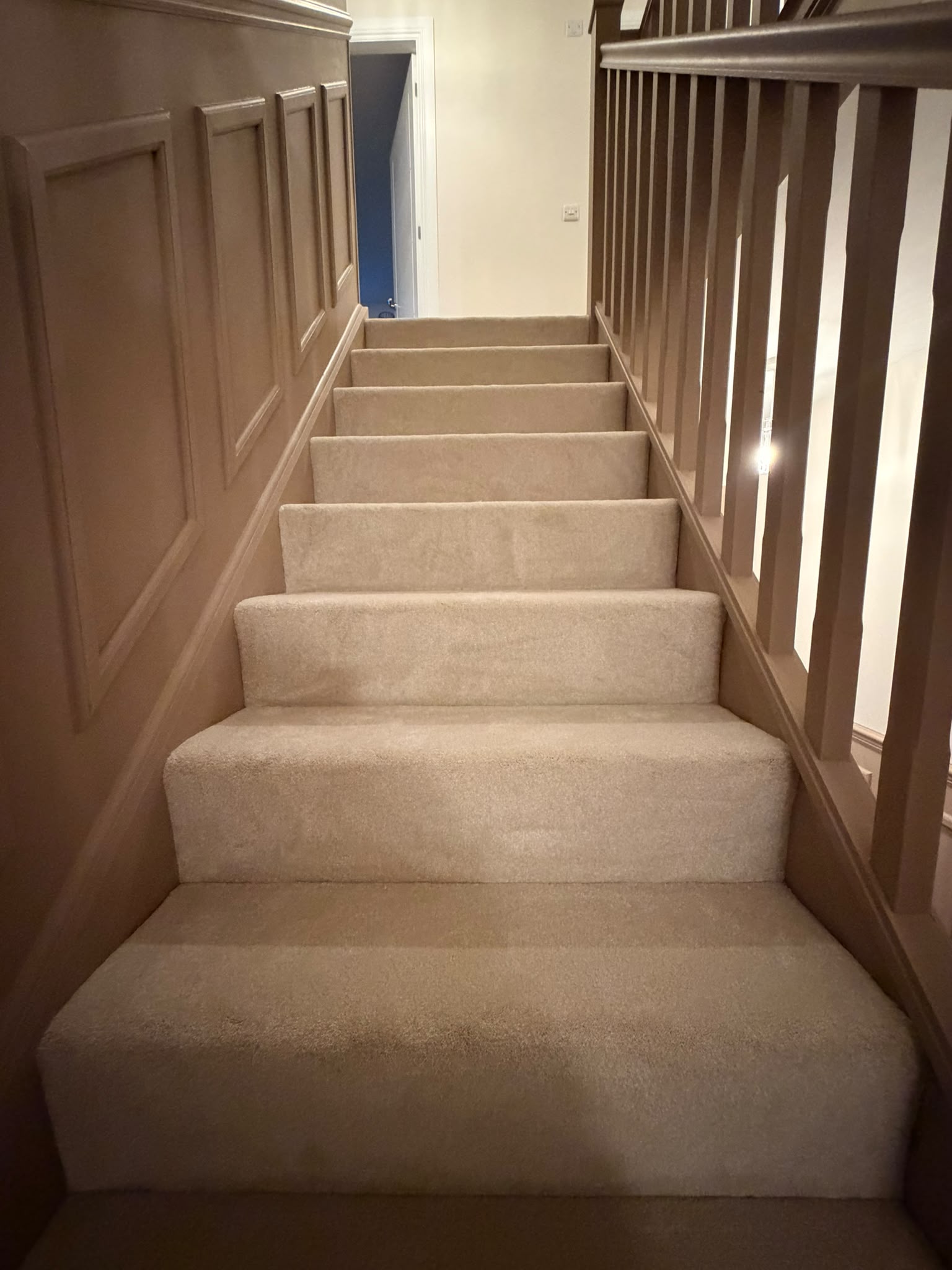 Cream carpet fitted to a staircase beside a panelled wall